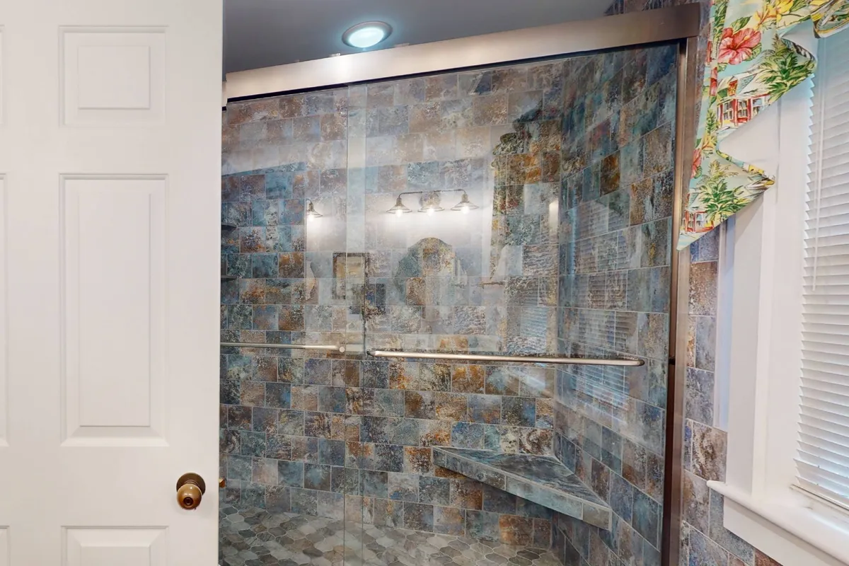 A serene ensuite bathroom featuring a glass shower enclosure, textured tile walls, built-in shower bench, and soft overhead lighting. The setting is designed for relaxation and rejuvenation, offering guests ultimate convenience and privacy.