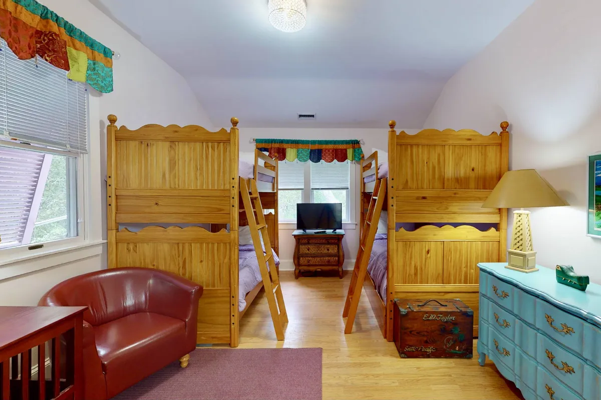 A cheerful interior space featuring colorful bunk beds, playful curtains, a cozy red armchair, and a blue dresser, creating a friendly and safe environment perfect for children. There's also a television, making it ideal for kids' downtime after a day of outdoor fun.