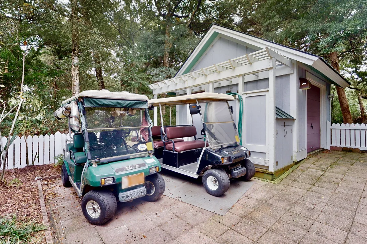 The image features two golf carts parked beside a tidy shed and a white picket fence, evoking the leisurely convenience provided for exploring the island. The surrounding greenery and relaxed mood underscore the home's readiness for adventure.