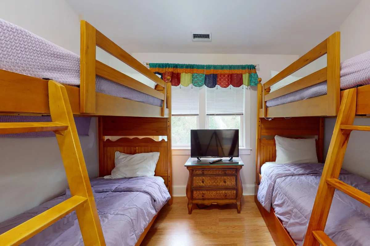 A playful children's bunk room with sturdy bunk beds, a TV for entertainment, wooden furniture, and a window that brings in natural light. The space feels relaxed and fun, perfect for kids' sleepovers and bonding moments.