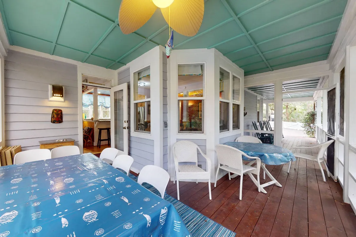 The dining area is defined by a large wooden table draped in a blue tablecloth, surrounded by white chairs and topped with a modern ceiling fan with wooden blades. The room feels bright and cheerful, ideal for family meals, social gatherings, or relaxing with friends after a day out.