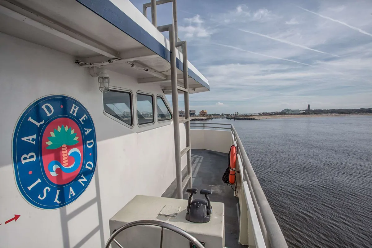 A boat deck featuring the Bald Head Island logo, overlooking the water. The scene highlights the thrill of arriving by boat and the promise of island adventures, with the possibility of spotting local wildlife or catching a beautiful sunset.