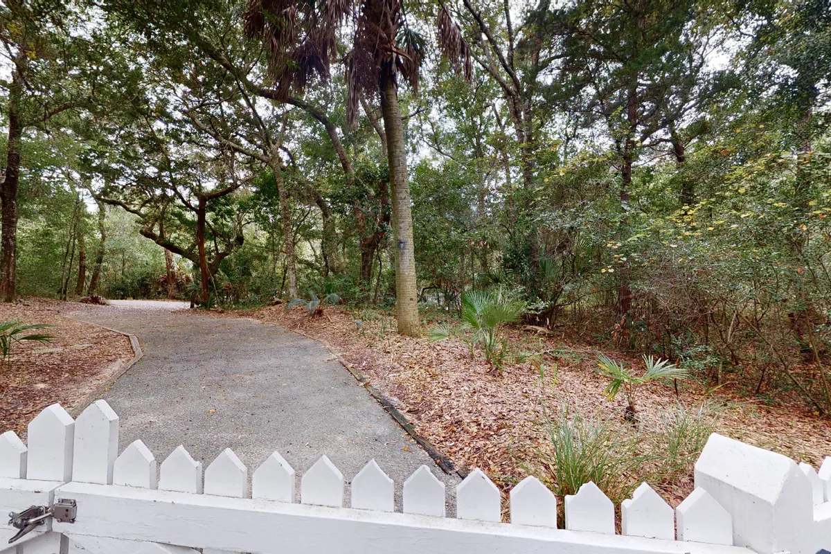 A peaceful exterior scene featuring a gravel pathway leading through a fenced entrance surrounded by lush greenery. The fence highlights security and access to nature, while the natural landscaping invites exploration and outdoor adventures with pets.