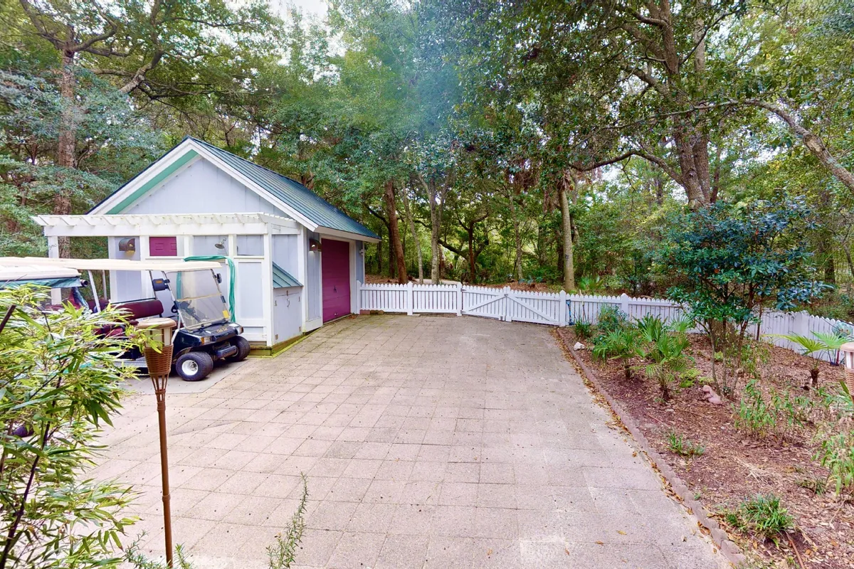 A charming cottage nestled among lush greenery, with a visible golf cart parked outside and comfortable seating on the porch. The scene highlights the convenience of island living, easy access by golf cart, and inviting outdoor relaxation spaces.